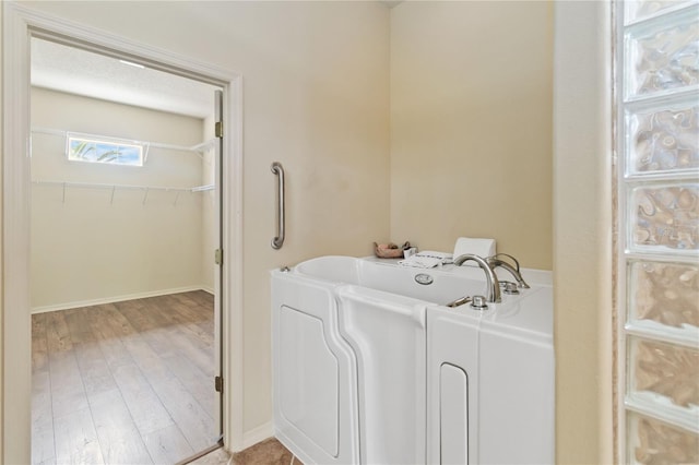 bathroom with baseboards, a walk in closet, a garden tub, and wood finished floors