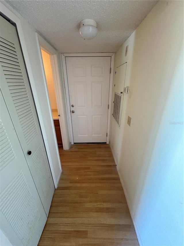 hall with baseboards, a textured ceiling, and light wood finished floors