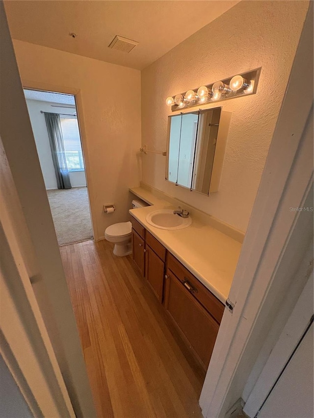 half bath with toilet, vanity, a textured wall, and wood finished floors