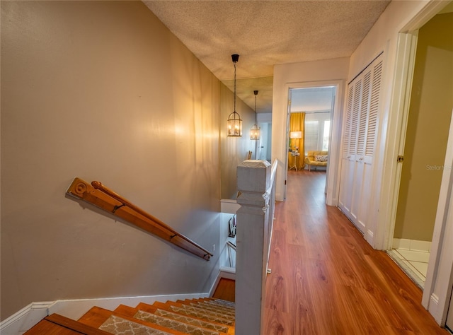 hallway with an upstairs landing, a notable chandelier, a textured ceiling, wood finished floors, and baseboards