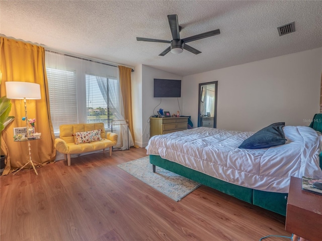 bedroom with visible vents, ceiling fan, vaulted ceiling, wood finished floors, and a textured ceiling