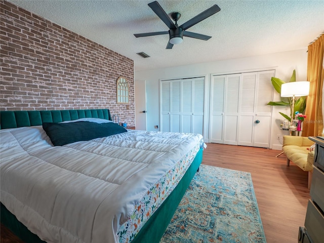 bedroom with wood finished floors, visible vents, brick wall, multiple closets, and a textured ceiling