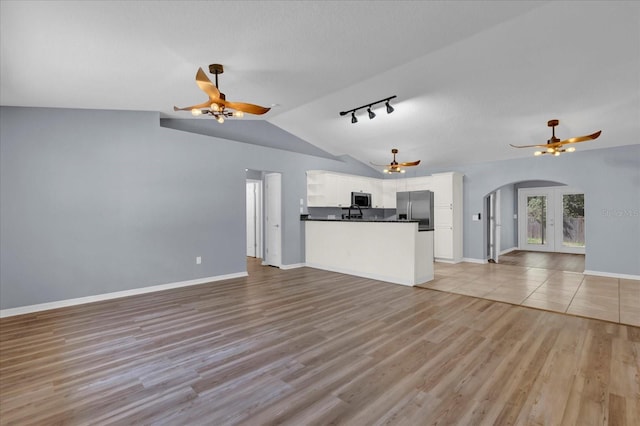 unfurnished living room with a ceiling fan, lofted ceiling, arched walkways, light wood-style floors, and french doors