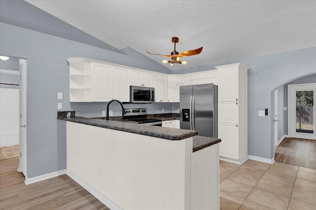 kitchen with a peninsula, open shelves, arched walkways, stainless steel appliances, and dark countertops