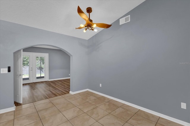 spare room featuring tile patterned flooring, baseboards, lofted ceiling, arched walkways, and a ceiling fan