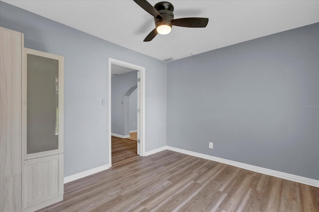 spare room with a ceiling fan, wood finished floors, baseboards, and arched walkways