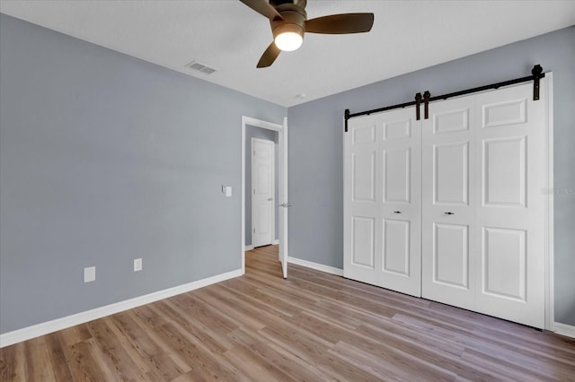 unfurnished bedroom featuring visible vents, wood finished floors, a barn door, baseboards, and ceiling fan