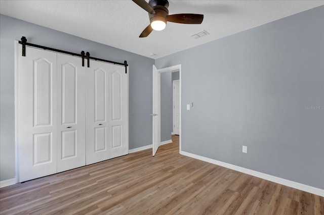 unfurnished bedroom with visible vents, baseboards, a barn door, light wood-style floors, and a closet