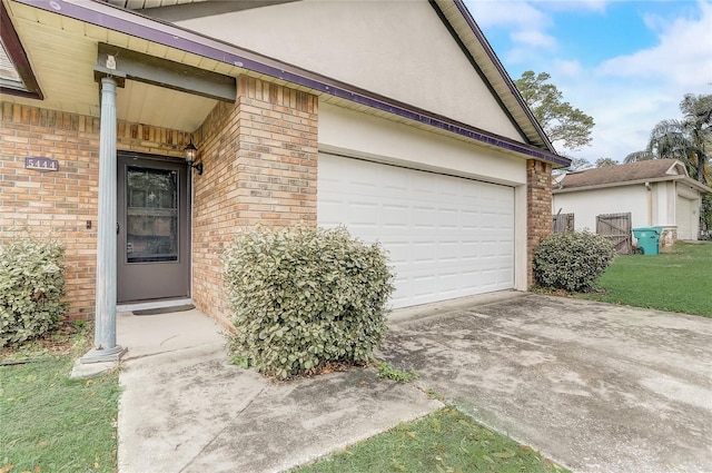 property entrance featuring stucco siding, brick siding, a garage, and driveway