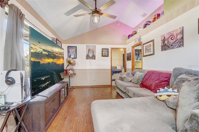 living area featuring visible vents, a wainscoted wall, light wood-style flooring, a ceiling fan, and vaulted ceiling