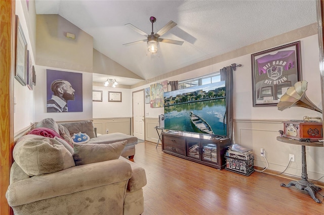 living area featuring a ceiling fan, wood finished floors, wainscoting, vaulted ceiling, and a textured ceiling