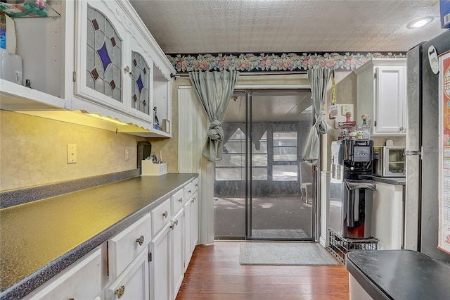 kitchen featuring wood finished floors, a toaster, glass insert cabinets, white cabinetry, and dark countertops