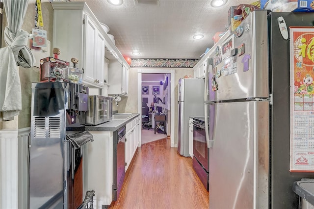 kitchen with light wood finished floors, range with electric stovetop, freestanding refrigerator, white cabinetry, and a sink