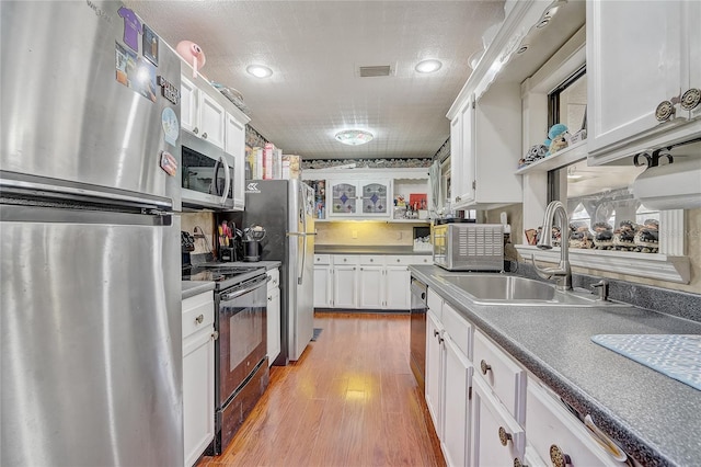 kitchen featuring light wood finished floors, visible vents, stainless steel appliances, white cabinetry, and a sink