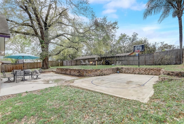 view of yard featuring basketball hoop, a fenced backyard, and a patio area