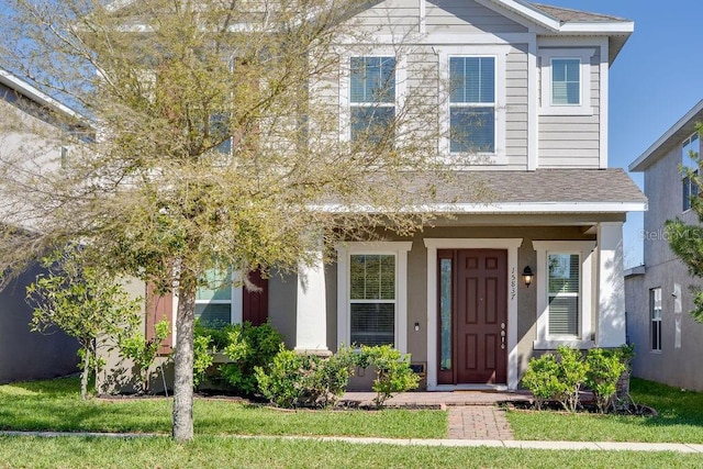 view of front of property featuring stucco siding, a shingled roof, and a front lawn