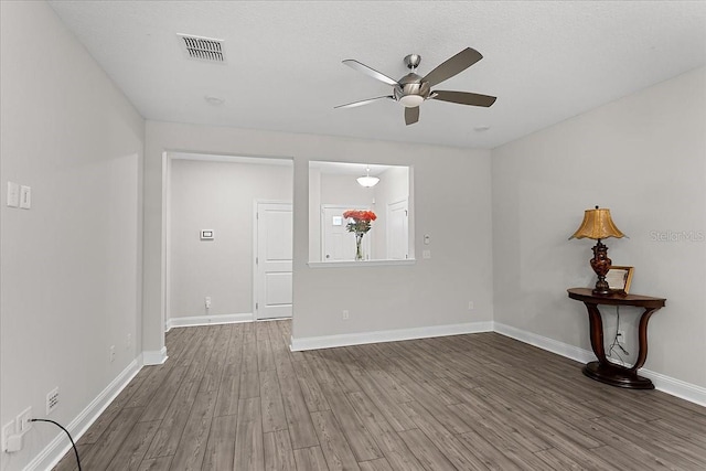 empty room with a ceiling fan, visible vents, wood finished floors, and baseboards