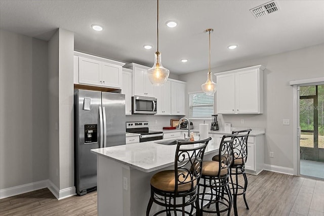 kitchen featuring light wood finished floors, an island with sink, a sink, appliances with stainless steel finishes, and white cabinetry