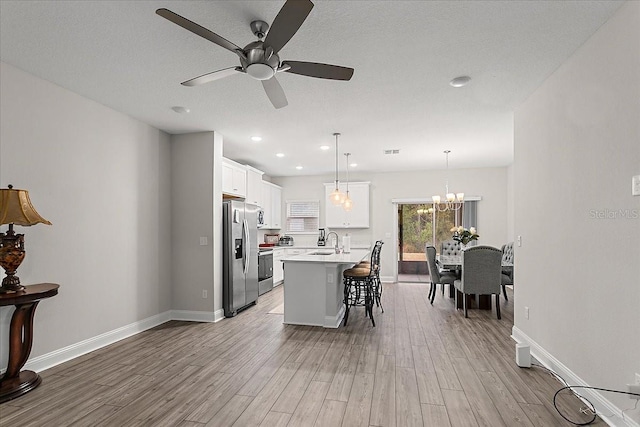 kitchen with a breakfast bar area, wood finished floors, a kitchen island with sink, a sink, and stainless steel refrigerator with ice dispenser