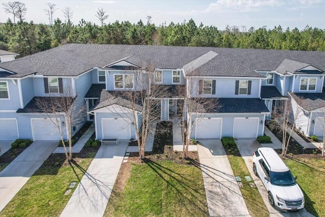 traditional home featuring a garage, a front yard, driveway, and a shingled roof