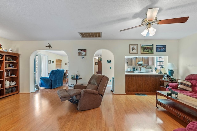 living area with arched walkways, visible vents, light wood-style flooring, and ceiling fan