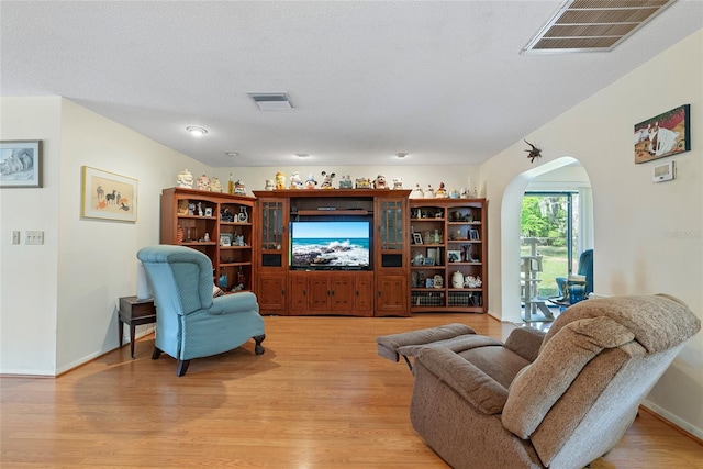 living area with arched walkways, visible vents, and light wood-style floors