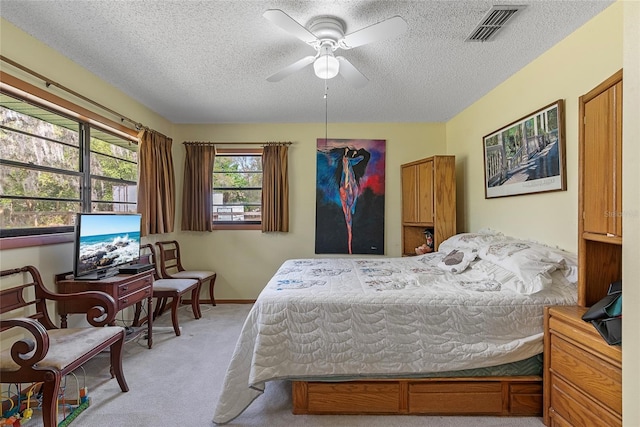 bedroom with visible vents, light colored carpet, ceiling fan, and a textured ceiling