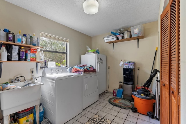 clothes washing area with a sink, a textured ceiling, separate washer and dryer, light tile patterned floors, and laundry area