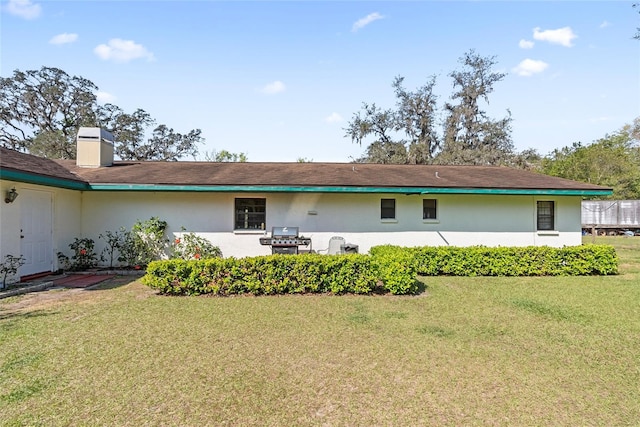 rear view of property featuring stucco siding, a lawn, and a chimney