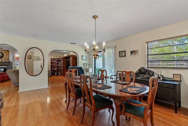 3634 Apfel Rd, Wesley Chapel, FL 33543 - dining space featuring arched walkways, a chandelier, light wood finished floors, a textured ceiling, and a glass covered fireplace