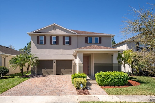 traditional-style home with a front lawn, decorative driveway, an attached garage, and stucco siding