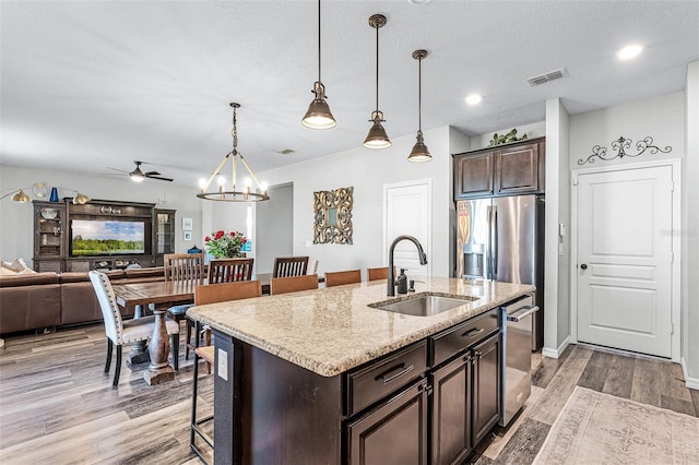 kitchen with visible vents, a breakfast bar, a sink, open floor plan, and dark brown cabinetry