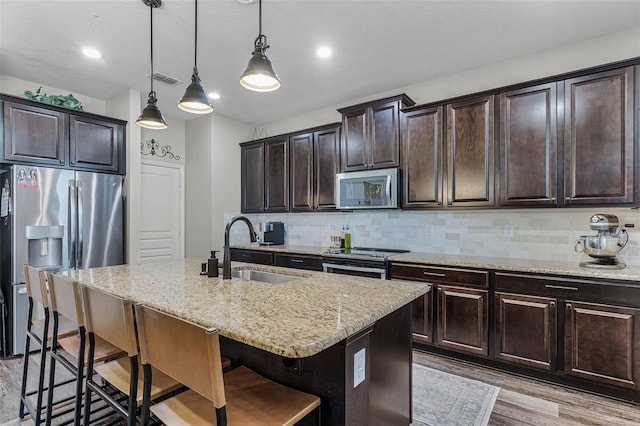 kitchen featuring light stone countertops, a breakfast bar area, decorative backsplash, appliances with stainless steel finishes, and a sink