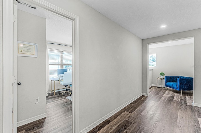 hallway featuring visible vents, wood finished floors, baseboards, and a textured ceiling