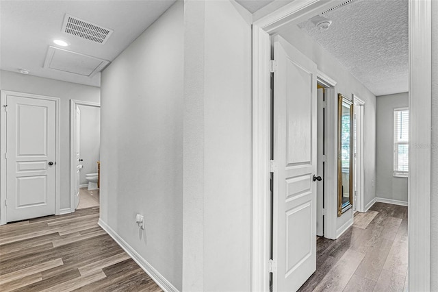 hallway with visible vents, baseboards, attic access, and wood finished floors