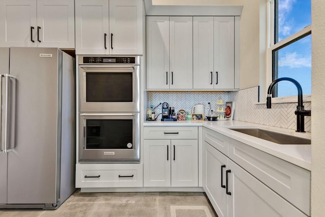 kitchen with backsplash, light countertops, appliances with stainless steel finishes, white cabinetry, and a sink