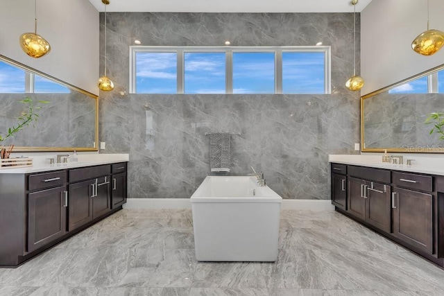 bathroom with a sink, marble finish floor, a freestanding tub, and two vanities