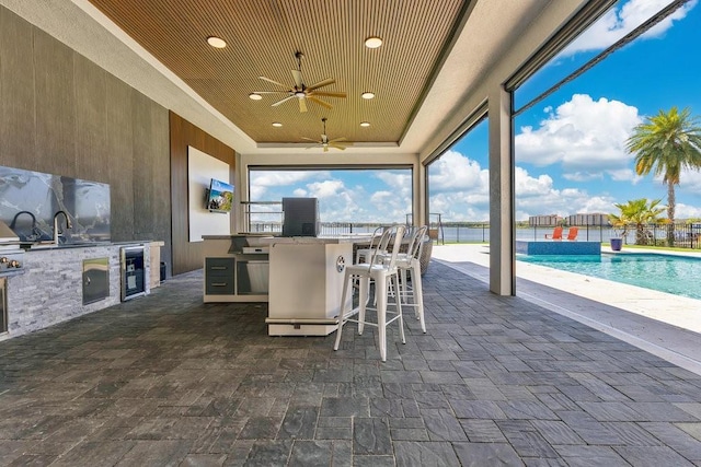 view of patio with a ceiling fan, a fenced in pool, fence, an outdoor kitchen, and outdoor wet bar