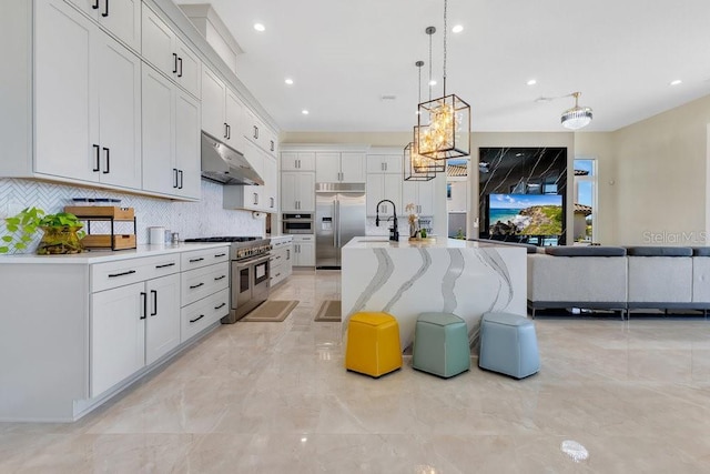 kitchen with a notable chandelier, under cabinet range hood, decorative backsplash, high end appliances, and hanging light fixtures