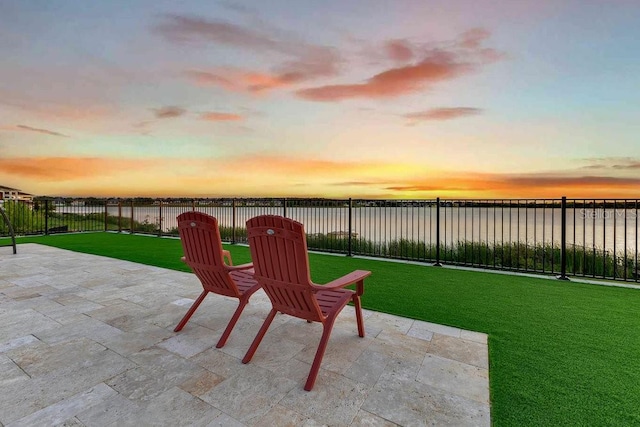 patio terrace at dusk featuring a lawn and fence