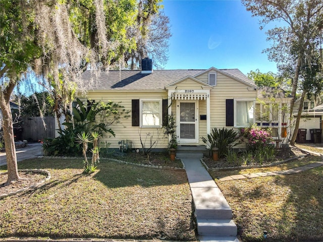 bungalow-style house with fence, a front yard, a shingled roof, central AC unit, and a chimney