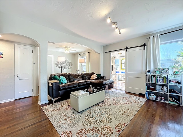 living room featuring arched walkways, dark wood-style floors, ceiling fan, and a barn door