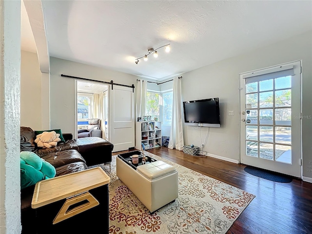 living room featuring a barn door, baseboards, a textured ceiling, and wood finished floors