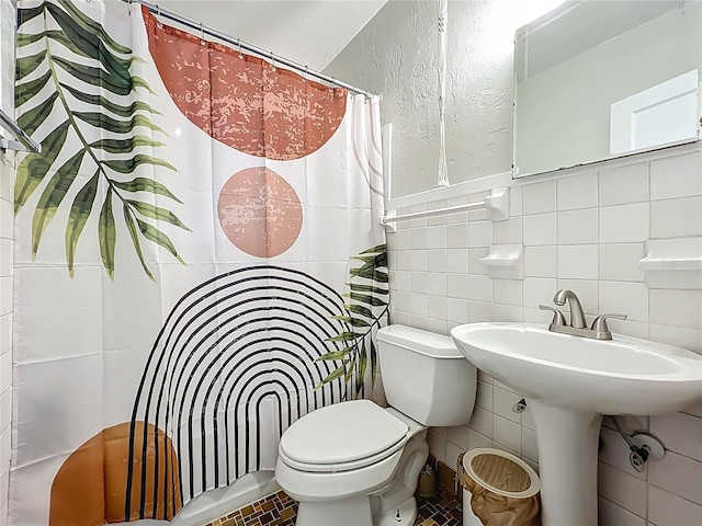 bathroom with curtained shower, tile walls, toilet, and a sink