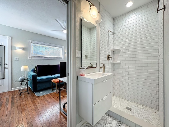 bathroom featuring ceiling fan, vanity, tiled shower, a textured ceiling, and wood-type flooring