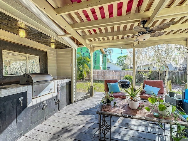 wooden deck featuring area for grilling, exterior kitchen, ceiling fan, and fence