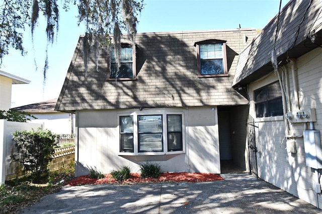 exterior space featuring mansard roof, roof with shingles, and fence