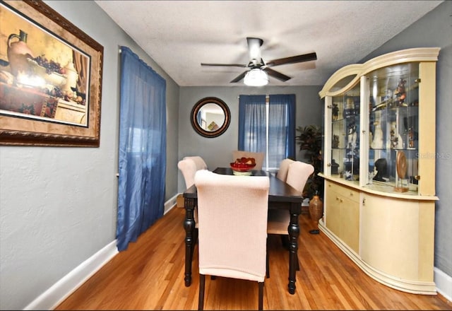 dining area with ceiling fan, a textured ceiling, baseboards, and wood finished floors