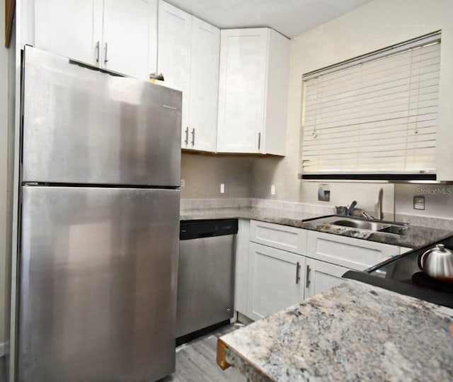 kitchen featuring light stone counters, appliances with stainless steel finishes, wood finished floors, white cabinetry, and a sink