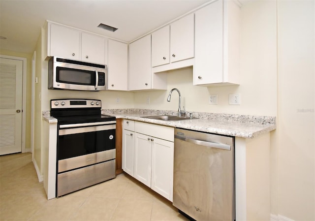 kitchen with a sink, stainless steel appliances, light tile patterned floors, and white cabinetry